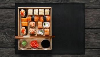 Japanese food restaurant, sushi maki gunkan roll plate or platter set. Free, copy space, chopsticks, ginger, soy sauce, wasabi. Sushi at rustic wood background in take away, delivery box. Top view. photo