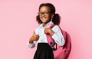 African American School Girl Gesturing Thumbs Up Posing With Backpack And Smiling Over Yellow Studio Background. I Like School photo