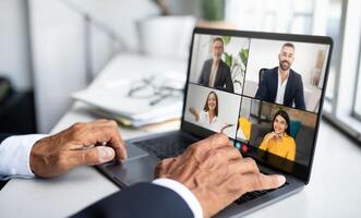 Four professionals are engaged in a virtual meeting using a laptop, discussing business strategies and plans. Participants appear focused and cooperative, ensuring effective communication photo