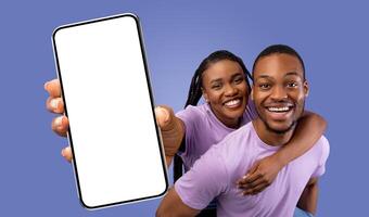 A happy black couple poses for a picture while holding up a smartphone with a blank screen. They are both smiling and looking at the camera. photo