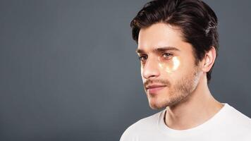 Young man with golden patches under eyes from wrinkles and dark circles, grey studio background photo