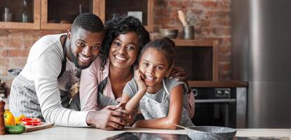 Cheerful black family spending time together at kitchen, looking at camera and smiling photo