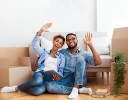 Relocation. Happy African American Couple Using Tablet Computer Discussing Interior Ideas Sitting Among Moving Boxes In New Home photo
