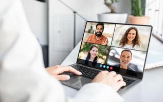 Lady sitting at a laptop is engaged in a conference with a group of people displayed on the screen. The individual appears focused as they interact digitally with their remote team. photo