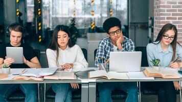Diverse students studying in university library with gadgets, preparing for classes photo