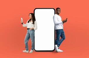 A man and woman are positioned next to a blank screen against an orange background. They are standing upright and appear to be focusing on the empty screen in front of them. photo