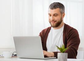 A man is seated in front of a laptop computer, focused on the screen with a serious expression. He is typing on the keyboard and appears to be working or studying intently. photo