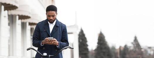 An African American businessman is commuting to the office on his bicycle while using his phone. The scene is energetic and dynamic, capturing the balance of modern work and active lifestyle. photo