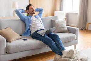 A middle-aged man is seen relaxing on a comfortable couch, engrossed in his laptop screen. He appears calm and focused as he works or browses the internet in a cozy indoor setting. photo