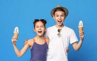 Happy little boy and girl embracing with ice cream cones, blue studio background photo