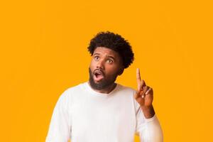 Young african american shocked man having idea, pointing finger up, got problem solution, orange studio background, empty space photo
