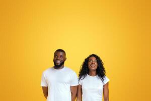 Delighted Black Couple Is Looking Upwards At Free Space, yellow studio background photo
