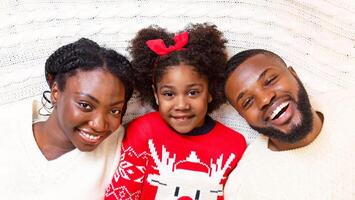 Christmas portrait. Joyful african american family of three lying on knitted blanket, top view photo