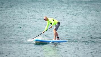 Man Sup Sea. Strong athletic man learns to paddle sup standing on board in open sea ocean on sunny day. Summer holiday vacation and travel concept. Aerial view. Slow motion video