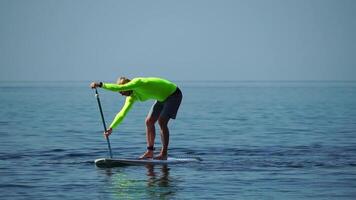 Sea man sup. Athlete man swimming in sea and paddleboarding at summer sunset. Healthy strong male enjoy outdoor active lifestyle and water sports on holiday vacation. Slow motion video