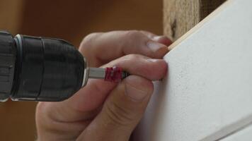 A man hands using a power tool fastens a board with a screw. Slow motion video