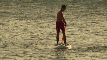 Man Paddleboarding Beach Watersports - A man paddleboards in shallow water on a sandy beach. video