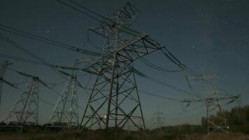 Nighttime view of high voltage power lines against the backdrop of moving stars in the night sky on a moonlit night. Concept of fuel and power generation video