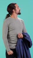 Vertical Man holding jacket in one hand while looking around, contemplating, creating a sense of curiosity. Person holding coat showing curiosity for surroundings, studio background, camera A video