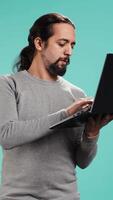 Vertical Man composing email, typing on laptop keyboard, excited to log off after work. Cheerful person sending mail online, brainstorming message idea, isolated over studio background, camera B video