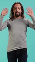 Vertical Smiling man greeting friends, happy to see them, isolated over blue studio background. Friendly person waving hand, saluting mates, being friendly, studio backdrop, camera A video