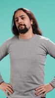 Vertical Portrait of man standing confidently with hands on hips, posing against plain studio background, projecting confidence and strength. Person holding assertive stance posture, camera B video