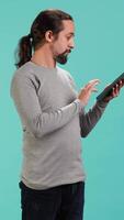 Vertical Man browsing though financial audit report on tablet, isolated over blue studio background. Worker reading paperwork on digital portable device, solving business tasks, camera A video