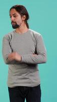 Vertical Portrait of man scratching neck with fingers, listening for unfamiliar sound, concentrating on finding source. Person tilting head, focusing on identifying noise, studio background, camera A video