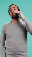 Vertical Man discussing with best friend over telephone call using smartphone, studio backdrop. Person talking with mate in phone call using cellphone, isolated over studio background, camera B video