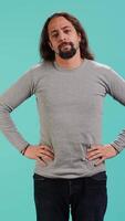 Vertical Portrait of man standing confidently with hands on hips, posing against plain studio background, projecting confidence and strength. Person holding assertive stance posture, camera A video