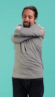 Vertical Portrait of man standing in studio, hugging himself in gesture of comfort and self love, isolated over studio background. Cheerful person doing self acceptance, embracing himself, camera A video