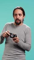 Vertical Portrait of gamer annoyed after losing online multiplayer videogame, being defeated by rival players. Man upset after seeing game over message, holding controller, studio background, camera B video