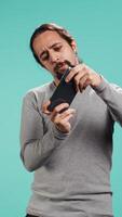 Vertical Delighted man playing videogames on smartphone, celebrating after being victorious against opponents online, studio backdrop. Player thrilled about winning game on mobile phone, camera B video