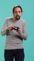 Vertical Portrait of gamer annoyed after losing online multiplayer videogame, being defeated by rival players. Man upset after seeing game over message, holding controller, studio background, camera A video