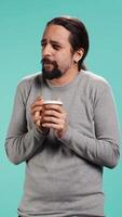 Vertical Man closes eyes while tasting and enjoying delicious coffee, isolated over blue studio backdrop. Person drinks caffeinated beverage to gain energy and be able to do doing productivity tasks, camera B video