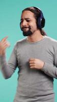 Vertical Happy person having fun, dancing on rhythm, listening music on headphones, enjoying leisure time. Cheerful man doing funky movements on songs, isolated over studio background, camera B video