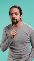 Vertical Portrait of man doing shushing hand gesturing, requesting silence. Person placing finger on lips, doing quiet sign gesture, asking for secrecy, isolated over studio background, camera B video