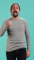 Vertical Man shaking fist in excitement while cheering for favorite sports team, isolated over studio background. Person showing intense enthusiasm expression and passion, supporting team during game, camera A video