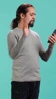 Vertical Portrait of smiling man talking with friends in phone call using smartphone, studio background. Jolly person feeling positive after receiving good news during telephone call, camera A video
