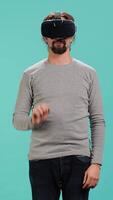 Vertical Man wearing virtual reality headset, interacting with interface, doing swiping motions. Person having fun using high tech futuristic modern VR gadget, isolated over blue studio background, camera A video