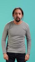 Vertical Portrait of frightened man covering his face with hands, standing isolated against studio background. Scared person with fearful facial expression suffering shock, feeling distraught, camera A video