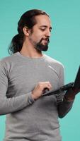 Vertical Man using laptop to do business related tasks for company, isolated over studio background. Office clerk doing budgeting, forecasting, and financial analysis on notebook, camera B video