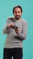 Vertical Cheerful player happy after winning gaming console game, shaking fist, studio background. Portrait of man satisfied after being victorious in videogame, defeating all enemies using gamepad, camera A video