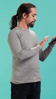 Vertical Portrait of upbeat person mindlessly scrolling on tablet screen, isolated over studio background. Cheerful man passing time on social media on portable device, enjoying leisure time, camera A video