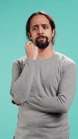 Vertical Pensive man deep in thoughts, doing ruminating hand gesturing, isolated over studio background. Unsure person doing stroking chin gesture, thinking, studio backdrop, camera B video