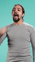 Vertical Man shaking fist in excitement while cheering for favorite sports team, isolated over studio background. Person showing intense enthusiasm expression and passion, supporting team during game, camera B video