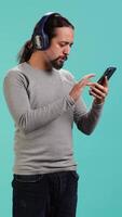 Vertical Relaxed man having fun listening to music from mobile phone, studio backdrop. Carefree person hearing tunes playing from smartphone device, isolated over studio background. camera A video