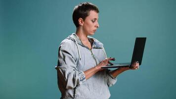 Casual woman browsing web on her laptop for freelance work in studio, remote network. Wireless computer user blogging on a new interface, trendy modern tech person. Camera A. video