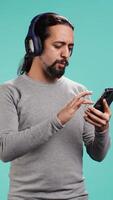 Vertical Relaxed man having fun listening to music from mobile phone, studio backdrop. Carefree person hearing tunes playing from smartphone device, isolated over studio background. camera B video