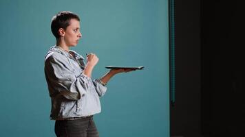 Modern tech person operating on tablet with a futuristic hologram, innovative visual graphics against blue background. Young woman looks at a holographic 3d image visualization. Camera A. video